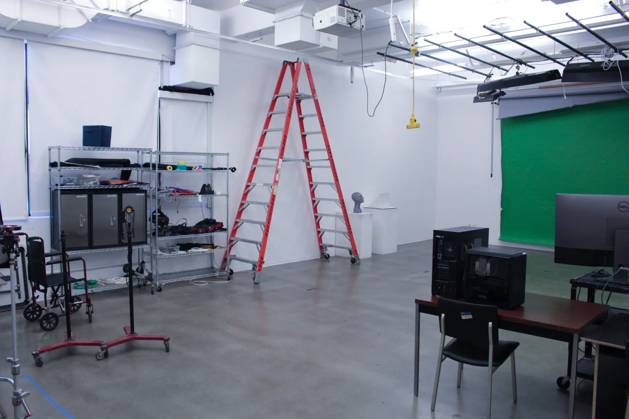 A photo studio with lights, ladder, green screen and computer.